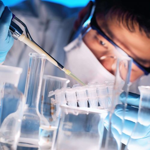 A young man adding liquid to a test tube